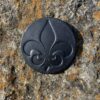 A black fleur de lis button on the side of a rock.