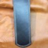 A black leather strap with white stitching on top of brown leather.