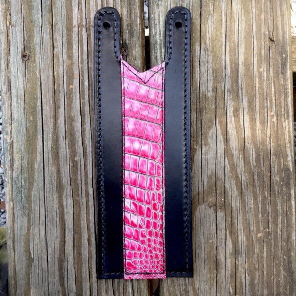 A pink and black leather strap hanging on a wooden wall.