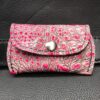 A pink and silver wallet sitting on top of a black leather bag.