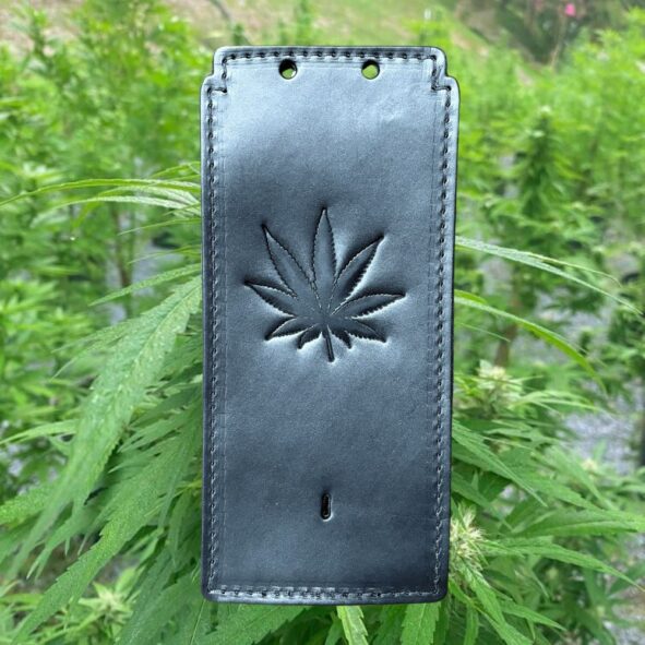 A black case with a leaf on it in front of some plants.